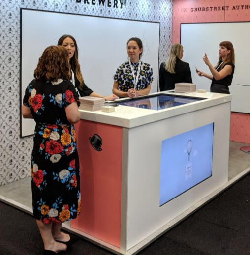 Five individuals standing at a tradeshow booth socializing.